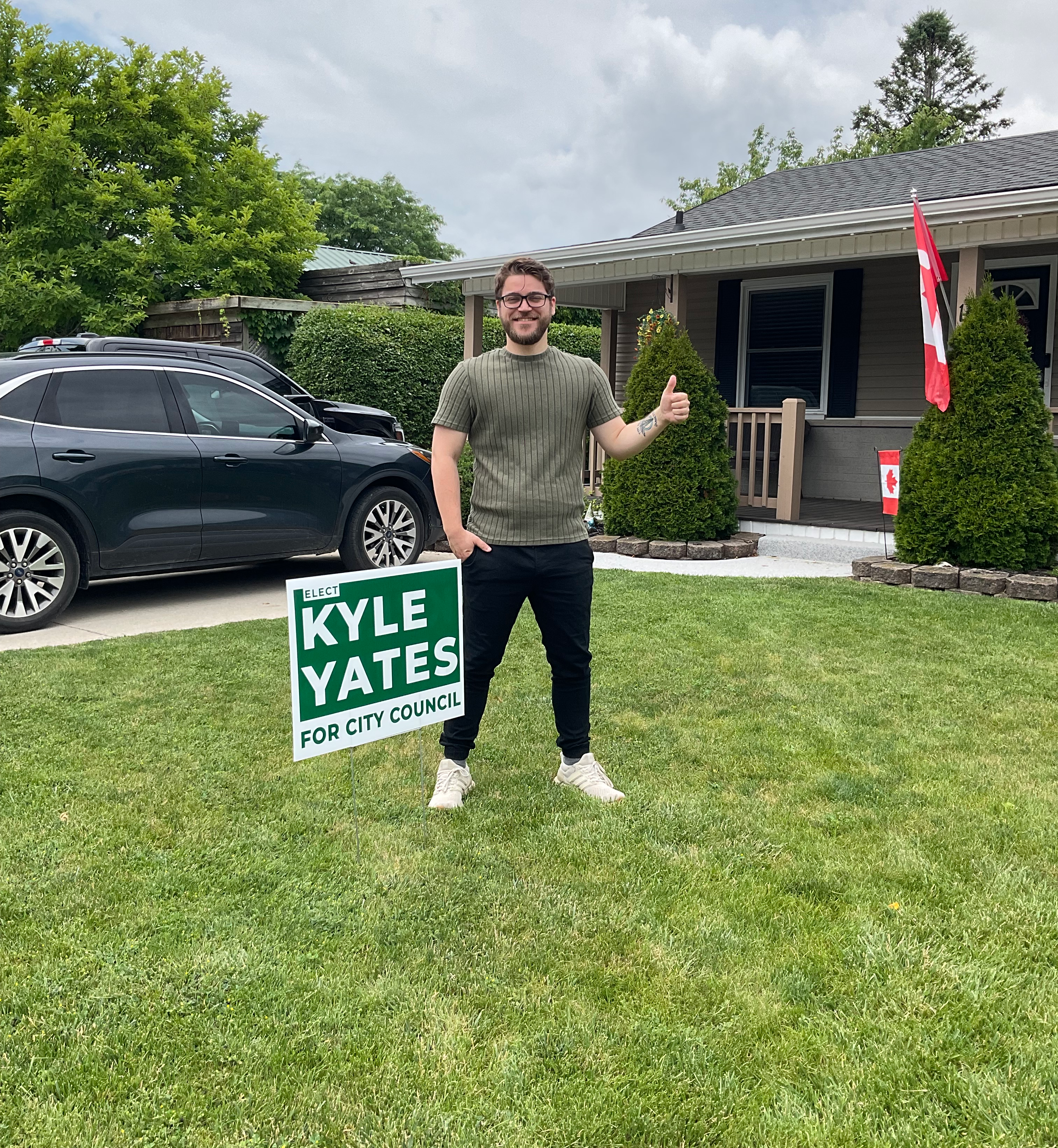 Kyle Yates standing on his front lawn next to an Elect Kyle Yates campaign sign